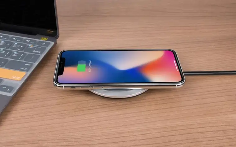 A smartphone charging on a wireless pad next to a laptop