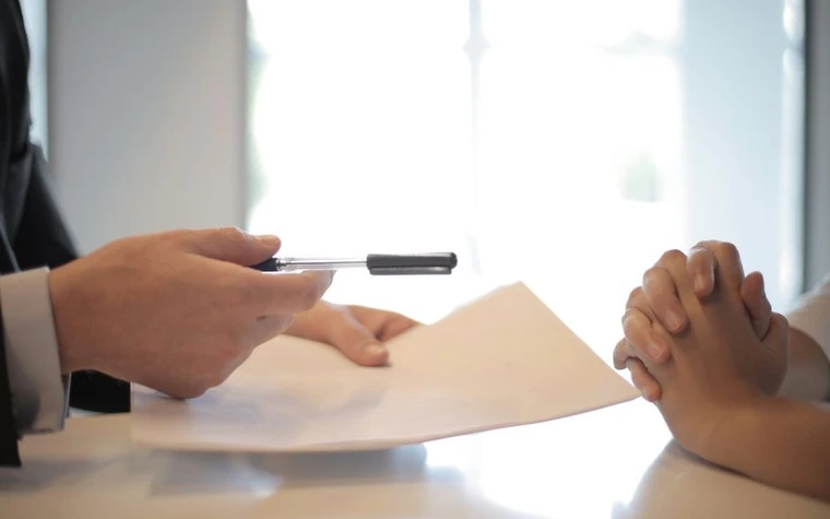 A hand passing a pen to sign a document