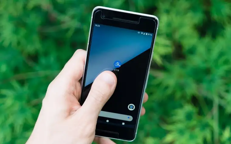 A hand tapping a smartphone home screen against a green blurred background