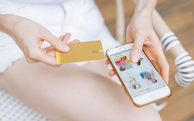 A hand holding a credit card next to another hand holding a smartphone