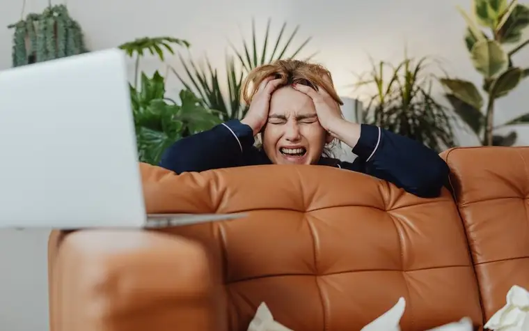 A woman leaning on a sofa with her hands on her head, looking frustrated