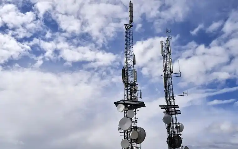 Two telecom towers with antennas and dishes under a cloudy sky