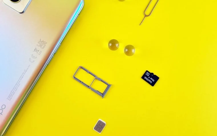 A close-up of a smartphone with a SIM tray, a memory card and a SIM card on a yellow background