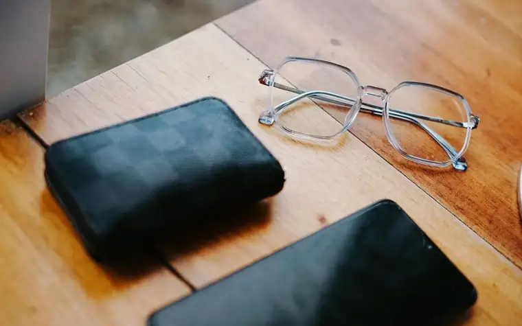 A wallet, glasses and a smartphone on a wooden table