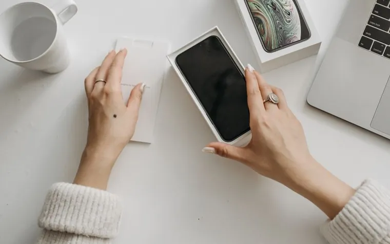 Hands opening a new smartphone box on a white desk
