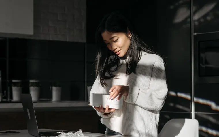 밝은 스웨터를 입은 여성이 주방에서 상자를 열어 물건을 꺼내는 모습