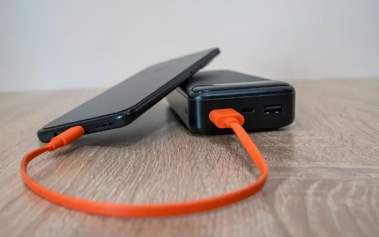 A smartphone connected by an orange cable to a power bank and charging